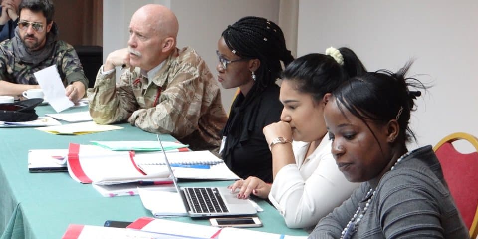 Autour d’une table de travail, des participantes et un officier en tenue examinent des dossiers pendant une épreuve.