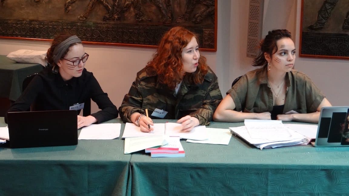 Trois participantes en tenue de terrain, dossiers et carnets ouverts, délibèrent derrière une table.